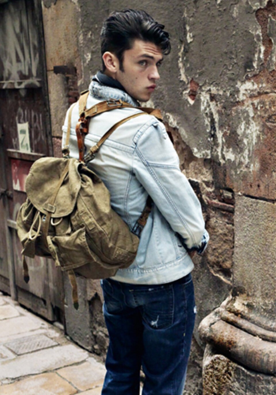 Junger Mann mit Rucksack steht an einer Wand
